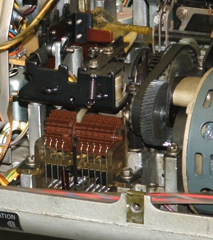 Figure 3 — A teleprinter answerback mechanism: a drum of code-cut sheet-metal tabs that transmits one fixed identifying message when the HERE IS function is tripped. It is a read-only memory cut from metal, a…